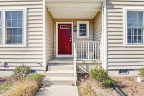 Une maison à deux étages avec une porte rouge, des balustrades blanches et un petit porche.
