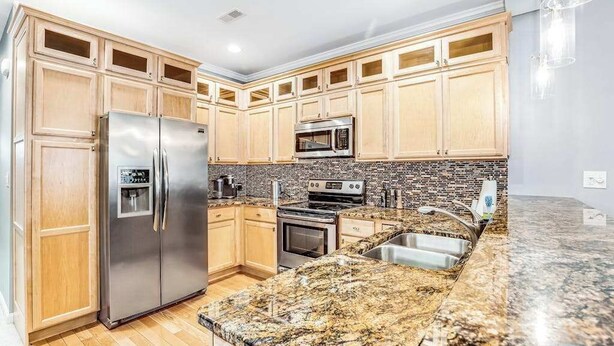 Una cocina con armarios de madera, electrodomésticos de acero inoxidable, encimera de granito y salpicadero de azulejos.