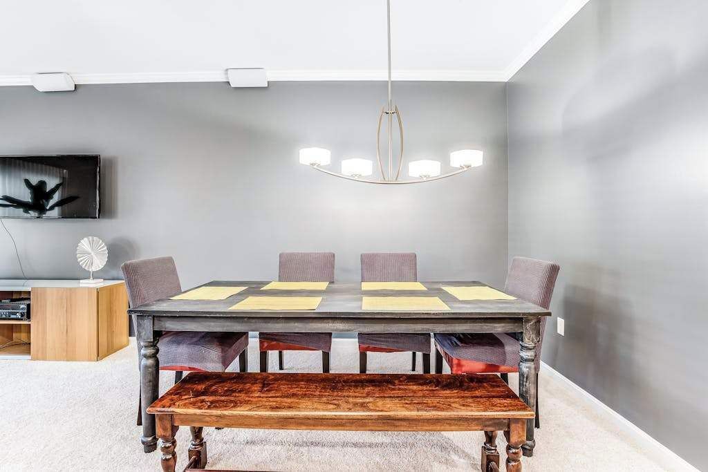 Un espace repas comprenant une longue table, des chaises, un banc, un lustre et un téléviseur fixé au mur.