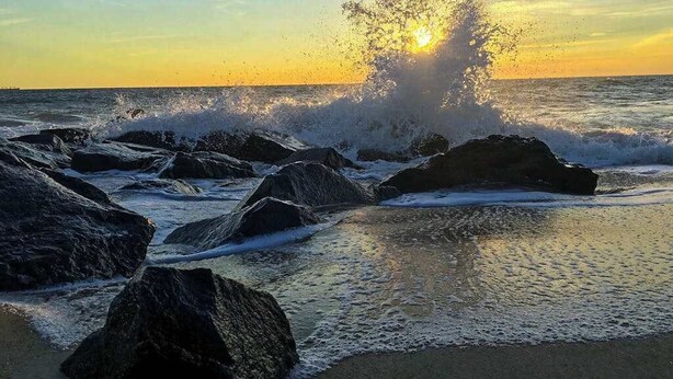 Una playa con rocas grandes y olas rompiendo sobre la orilla.