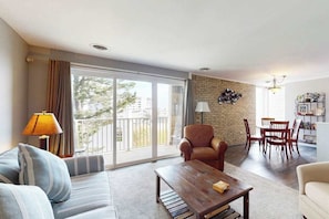 Un salon comprenant un canapé, un fauteuil, une table basse, une table à manger, des chaises et un balcon avec des rideaux.