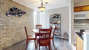 Un comedor con pared de ladrillo, sillas de madera, una mesa redonda y una lámpara colgante.