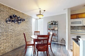 Un espace repas avec un mur en briques, des chaises en bois, une table ronde et un luminaire suspendu.