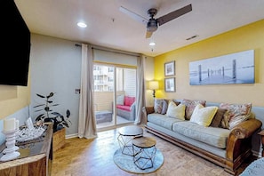 A living room with a sofa, a coffee table, a ceiling fan, and a large window with curtains.