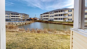 A view of a residential building complex with a small pond in the foreground. - The Palms water-view condo near beach with outdoor pool, streaming, W/D, & AC (Rehoboth Beach)