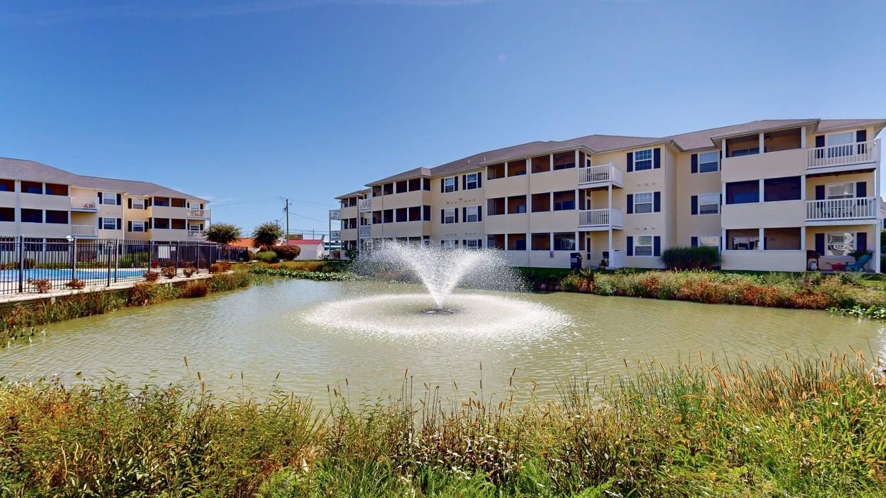 A multi-story building with balconies, a central water feature, and a landscaped area with vegetation.