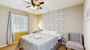 A hotel room with a bed, a chair, a nightstand, a lamp, and a ceiling fan. - The Palms water-view condo near beach with outdoor pool, streaming, W/D, & AC (Rehoboth Beach)