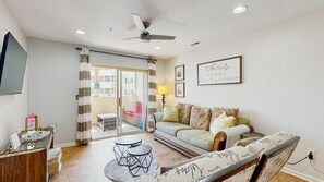 A living room with a sofa, a coffee table, a TV, and a ceiling fan. - The Palms water-view condo near beach with outdoor pool, streaming, W/D, & AC (Rehoboth Beach)