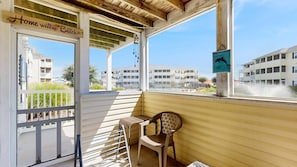 A covered balcony with a chair, a sign reading 'Home is where the beach is,' and a dolphin sign. - The Palms water-view condo near beach with outdoor pool, streaming, W/D, & AC (Rehoboth Beach)