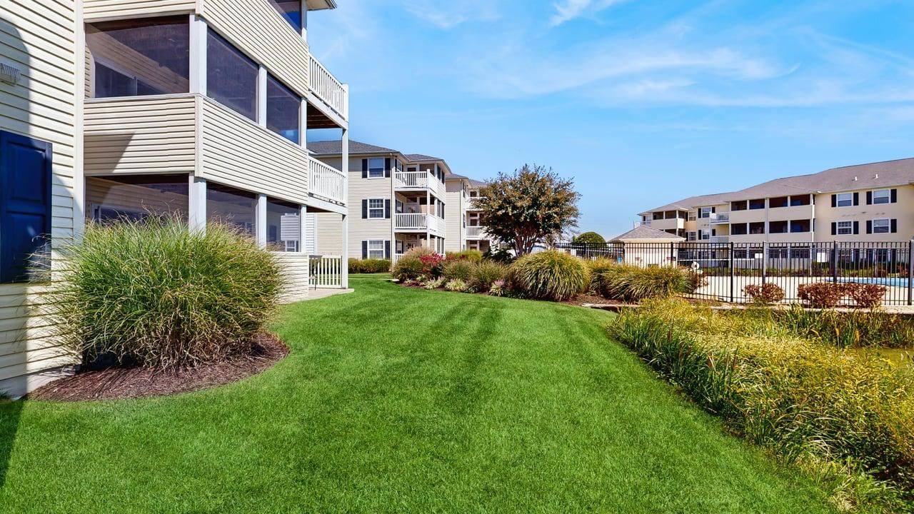 Een appartementencomplex met meerdere balkons, een verzorgd gazon en een omheind zwembad.