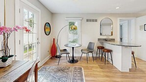 Una cocina moderna con una isla central, una zona de comedor con una mesa redonda y sillas, y un ventanal con persianas.