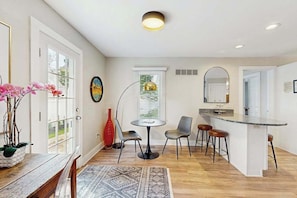 A modern kitchen with a central island, a dining area with a round table and chairs, and a large window with blinds. - Rehoboth Beach home near beach with decks, yard & W/D - dog-friendly (Rehoboth Beach)