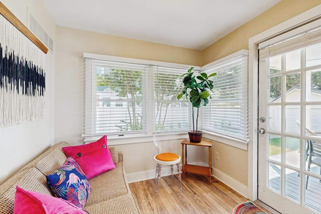 A corner room with a wicker sofa, a small stool, a potted plant, and a door leading outside.