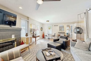 A modern living room with a fireplace, sofa, coffee table, and a TV mounted on the wall. - Rehoboth Beach home near beach with decks, yard & W/D - dog-friendly (Rehoboth Beach)
