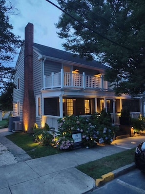 A two-story house with a porch, a chimney, and a front yard with flowers. - Rehoboth Beach home near beach with decks, yard & W/D - dog-friendly (Rehoboth Beach)