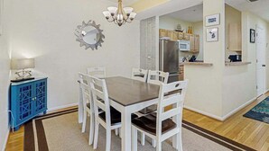 A dining area with a table and chairs, a chandelier, a mirror, and a kitchen in the background. - Eagles Landing comfy condo with pools and tennis courts - 1 mile to beach (Rehoboth Beach)