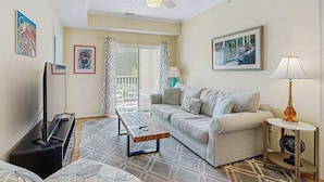 A living room with a sofa, coffee table, TV, and artwork on the walls. - Eagles Landing comfy condo with pools and tennis courts - 1 mile to beach (Rehoboth Beach)