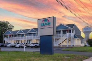 Un motel con temática de playa, con un letrero grande, varios balcones y un estacionamiento.