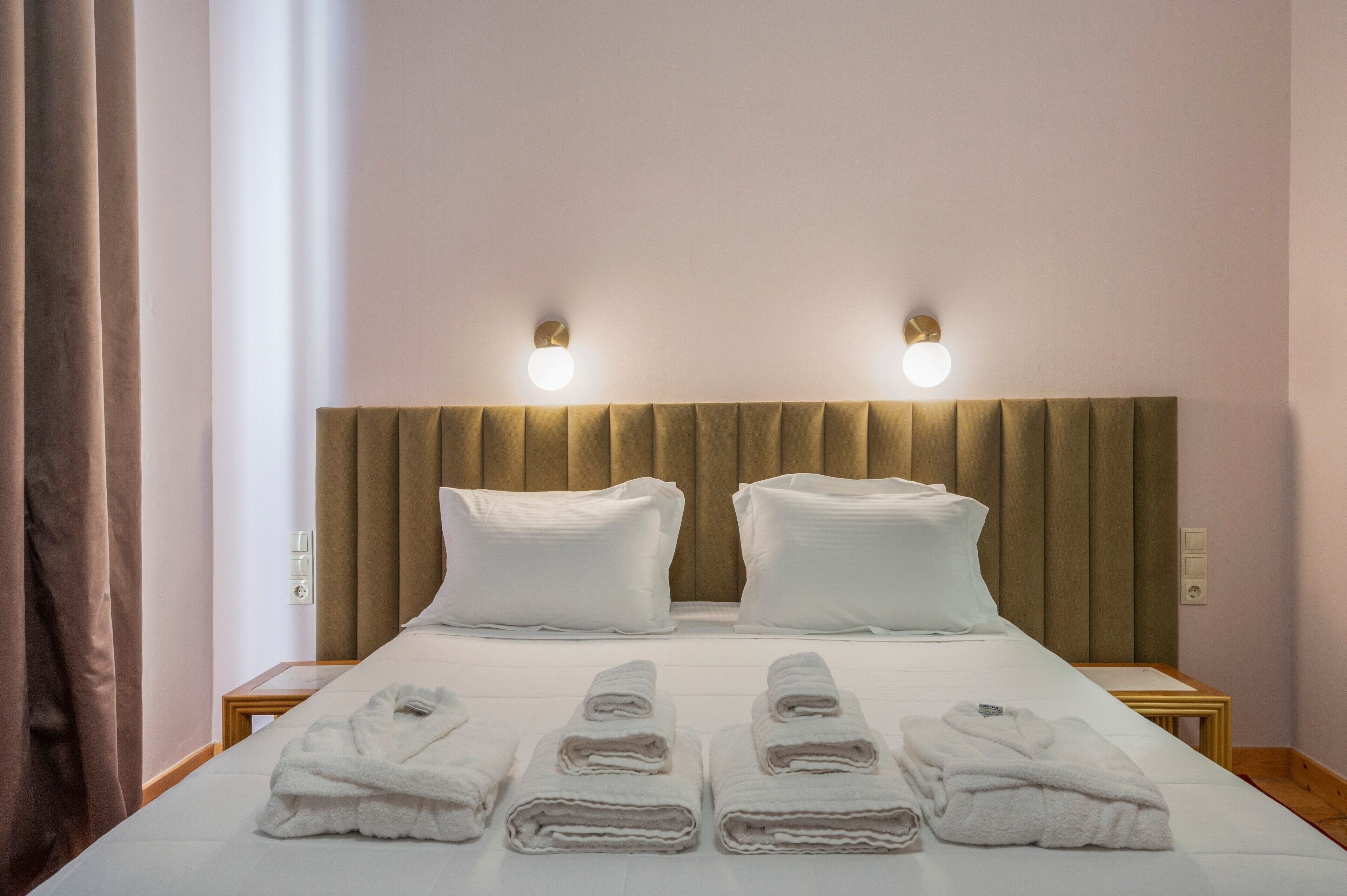 A hotel room with a bed, two bedside lamps, a headboard, and four towels on the bed.