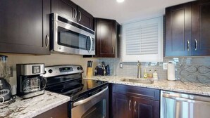 Una cucina moderna con mobili scuri, elettrodomestici in acciaio inossidabile, un piano di lavoro in granito e una finestra con persiane.