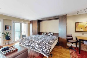 Ein Schlafzimmer mit Bett, Schreibtisch, Stuhl, Topfpflanze und einer Schiebetür.