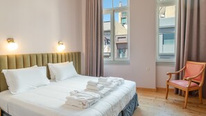 Ein Hotelzimmer mit Bett, Sessel, Fenster und Blick auf die Gebäude draußen.