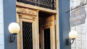 A hotel entrance with a wooden double door, a sign above the door, and a lamp on the wall. - Prince Antilochus – King-Size Bed Room with Balcony (Kalamata)