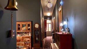 A hallway with a wooden cabinet, a clock, a red rug, and a desk with papers. - Prince Antilochus – King-Size Bed Room with Balcony (Kalamata)