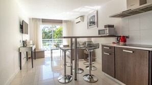 A modern kitchen with a dining area, stainless steel bar stools, a microwave, and a large window. - Two bedroom Croisette Apartment 61 (Cannes)