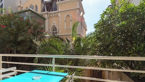 A balcony with a turquoise table, lush greenery, and a building with arched windows in the background. - Two bedroom Croisette Apartment 61 (Cannes)