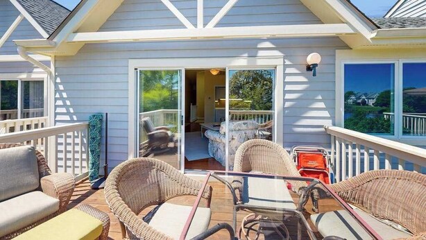 Un espacio al aire libre cubierto con mobiliario de mimbre, una mesa y vista hacia el interior de la vivienda.
