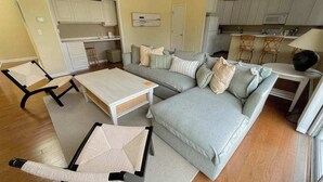 Sala de estar con sofá, una mesita de centro y una mesa de comedor. Se observa una zona de cocina con alacenas y un microondas.