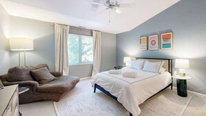 Un dormitorio con una cama, una silla, un ventilador de techo y obras de arte en la pared.