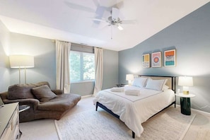Ein Schlafzimmer mit Bett, einem Sessel, einem Deckenventilator und Bildern an der Wand.