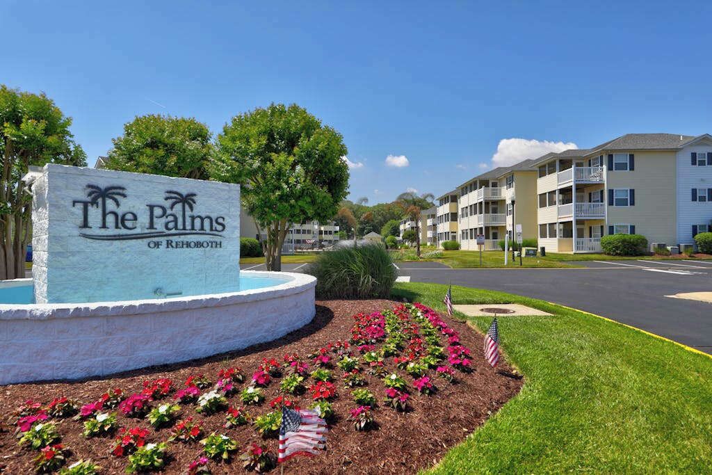 A sign for 'The Palms of Rehoboth' with a landscaped area and a road in the background.
