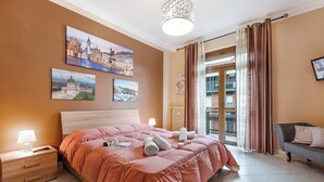 Een hotelkamer met een groot bed, een nachtkastje, een lamp, een bank en een balkon met gordijnen.