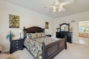 Quarto com cama, mesas de cabeceira, cômoda, ventilador de teto e obras de arte nas paredes.