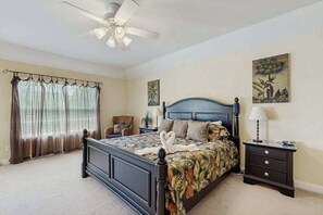 Une chambre à coucher avec un lit, une table de chevet, un ventilateur de plafond et une fenêtre avec des rideaux.