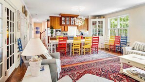 Amplia sala de estar con una mesa de comedor, sillas coloridas, un sofá y un tapete grande.