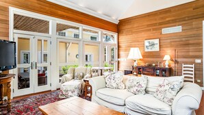 Una sala de estar con sofá, mesa de centro y televisor. Hay puertas que dan a un espacio exterior.