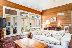 A living room with a sofa, coffee table, and a TV. There are doors leading to an outdoor area. - Rehoboth Beach North Shores home with pool, basketball, fast WiFi & W/D (Rehoboth Beach)