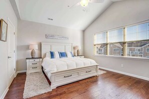 A bedroom with a large bed, two bedside tables, a white rug, a ceiling fan, and a window with blinds. - Dog-friendly condo near golf, pool, fireplace, central AC & private washer/dryer (Rehoboth Beach)