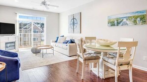 Un salon moderne comprenant un canapé, une table à manger, des chaises, un téléviseur et des œuvres d’art accrochées aux murs.