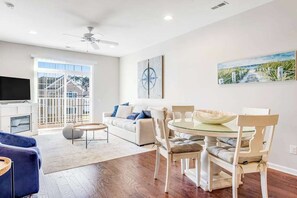 A modern living room with a sofa, dining table, chairs, a TV, and artwork on the walls. - Dog-friendly condo near golf, pool, fireplace, central AC & private washer/dryer (Rehoboth Beach)