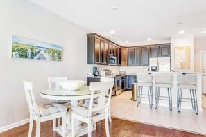 A modern kitchen with dark cabinets, a glass island, and a dining area with white chairs. - Dog-friendly condo near golf, pool, fireplace, central AC & private washer/dryer (Rehoboth Beach)