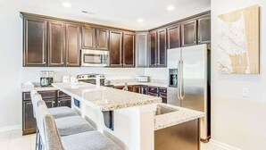 Une cuisine moderne avec des meubles en bois foncé, des appareils électroménagers en acier inoxydable et un îlot central doté d’un comptoir en granit.