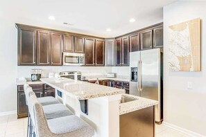 A modern kitchen with dark wood cabinets, stainless steel appliances, and a granite countertop island. - Dog-friendly condo near golf, pool, fireplace, central AC & private washer/dryer (Rehoboth Beach)