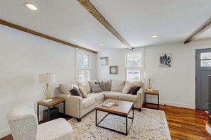 A living room with a sectional sofa, a coffee table, a patterned rug, and a wooden ceiling beam. - Town of Lewes Duplex w/deck, close to beach & restaurants (Lewes)