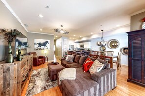 Ein geräumiger Wohnbereich mit einem großen braunen Ecksofa, einem Holzsideboard und einem Essbereich mit Holztisch und -stühlen.