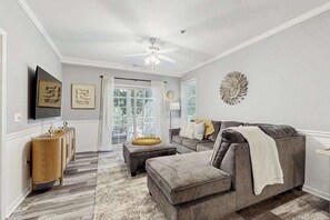 A living room with a grey sofa, ottoman, and a wooden side table. - The Tides spacious condo w/shared pool, close to restaurants & shopping (Rehoboth Beach)
